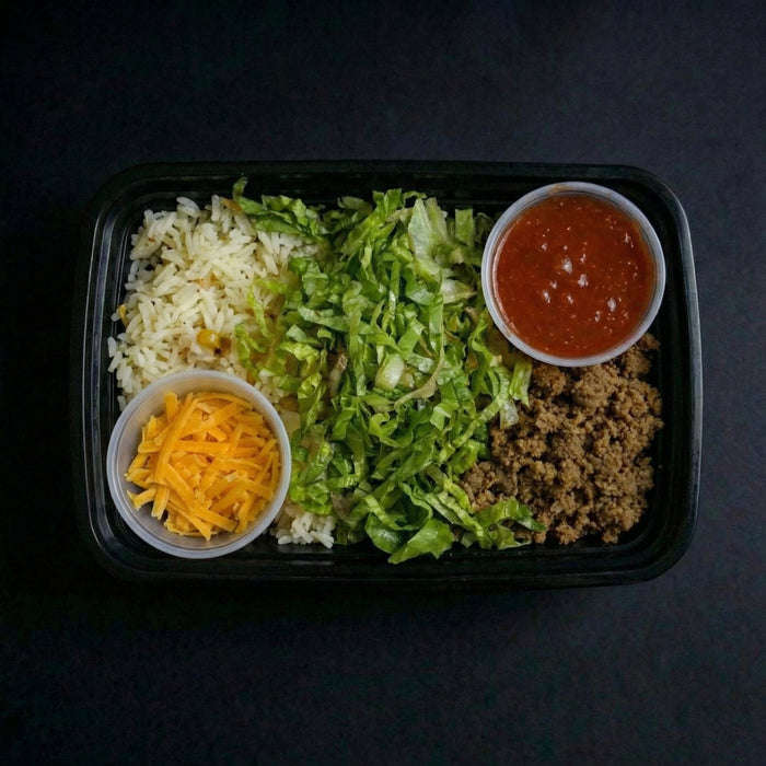 Prepared meal with rice, lettuce, ground meat, cheese, and sauce in a black container on a dark background
