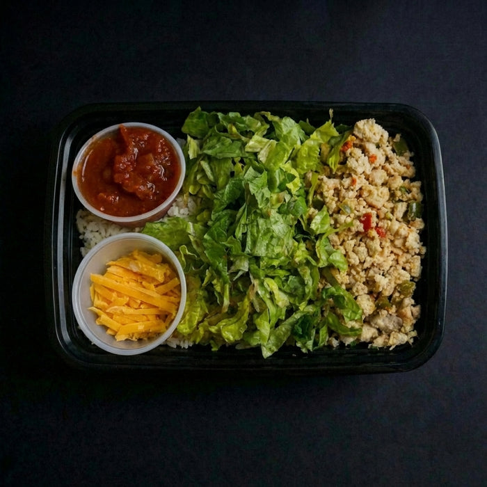 Prepared salad with lettuce, cheese, and dressing in a black container on a dark background