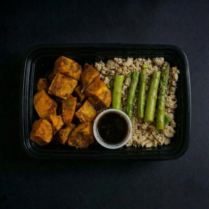 Plated meal with roasted sweet potatoes, asparagus, and a side of sauce on a dark background