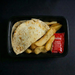 Plastic container with tortilla, fries, and ketchup packet on a dark background