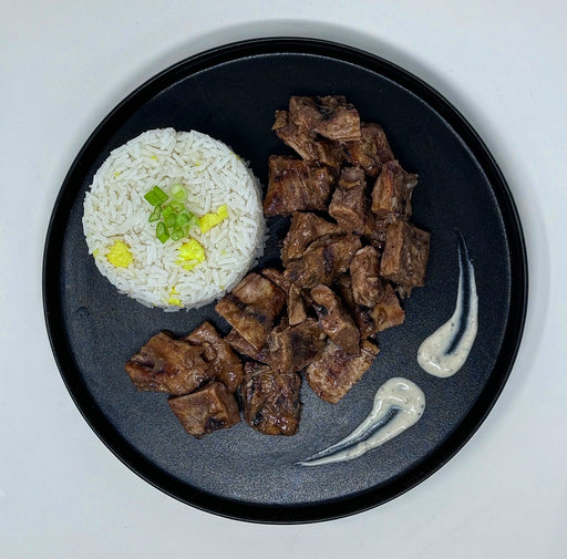Black plate with rice and guava teriyaki chicken chunks on a light gray background
