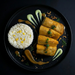 Plated dish with rolled food item, white rice, and green sauce on a dark background