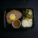 Meal in a black tray with meatloaf, egg, rice, and vegetables on a dark background