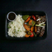 Plated meal with rice, vegetables, and meat on a dark background