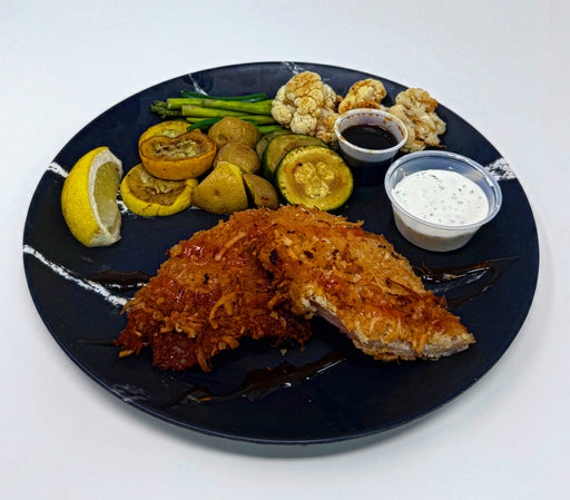 Plated dish with fried fish, vegetables, and sauces on a black plate.