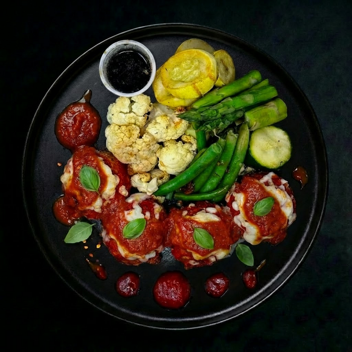 Plated dish with meatballs, vegetables, and a side of sauce on a dark background