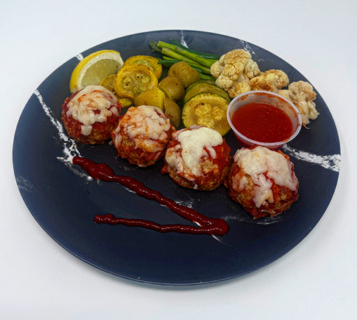 Plated dish with meatballs, vegetables, and a side of sauce on a white background. A low calorie meal made by spartan meal preps.