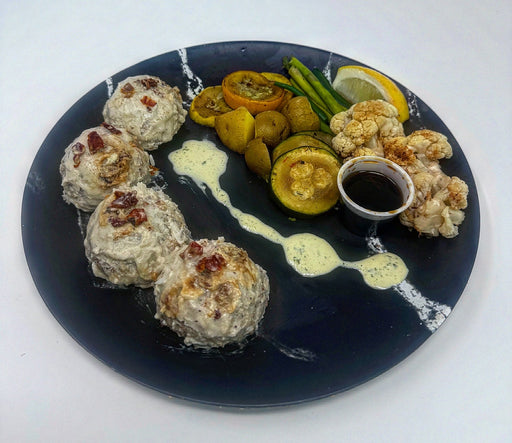 Plated dish with meatballs, vegetables, and a small bowl of sauce on a dark plate. A low calorie plate made by spartan meal preps.