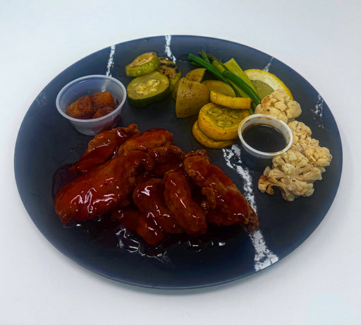 Plated dish with chicken wings, vegetables, and sauces on a dark plate. Made by Spartan Meal Preps, a NJ Meal Prep Delivery Company. 
