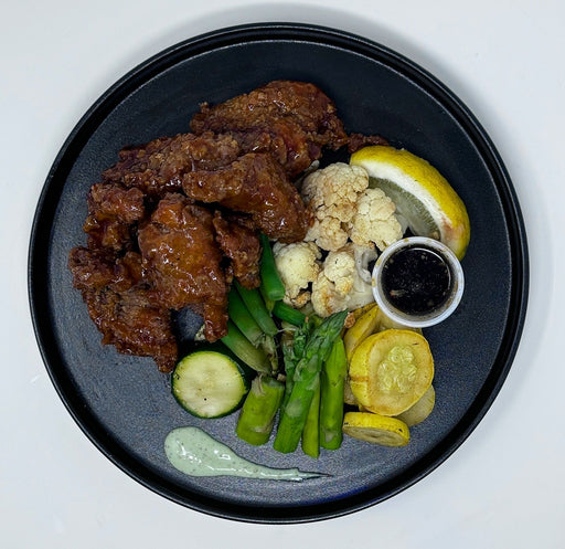 Plated dish with chicken wings, vegetables, and sauces on a dark plate. Made by Spartan Meal Preps, a NJ Meal Prep Delivery Company. 