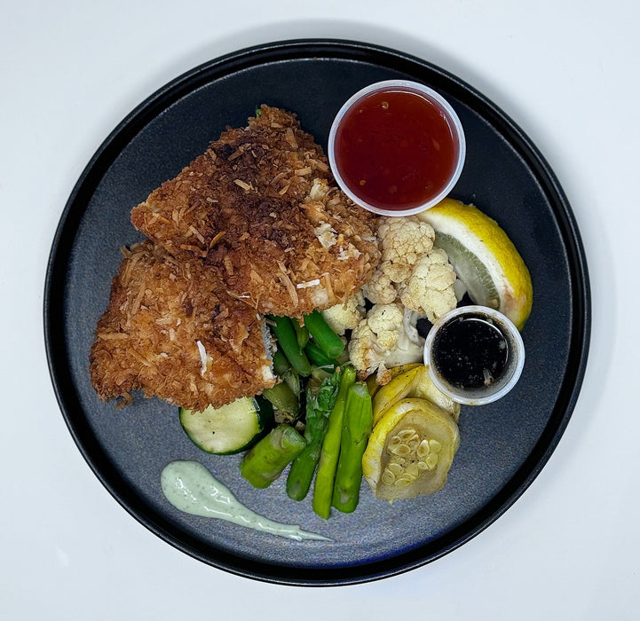 Plated dish with fried flounder, vegetables, and sauces on a black plate.