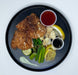 Plated dish with fried flounder, vegetables, and sauces on a black plate.
