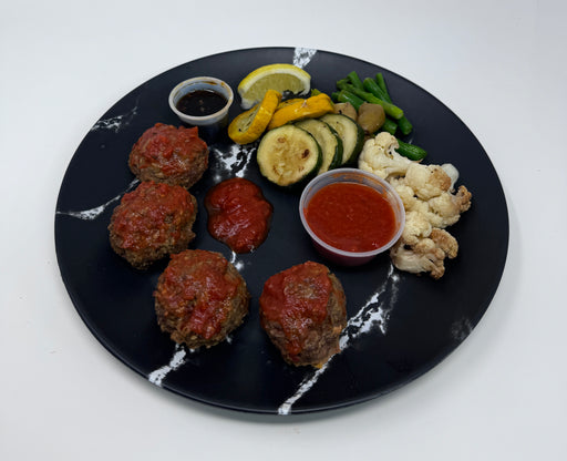 Black plate with meatballs, vegetables, and sauces on a white background