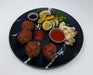 Black plate with meatballs, vegetables, and sauces on a white background