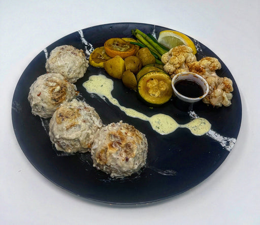 Plated dish with meatballs, vegetables, and a dipping sauce on a white background