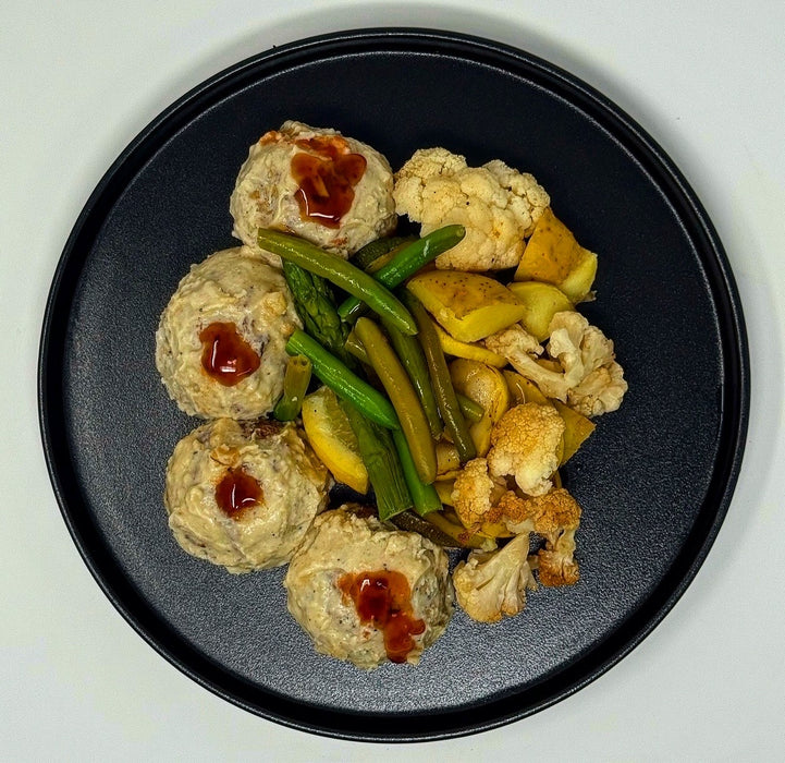 Black plate with meatballs, green beans, and cauliflower on a white background