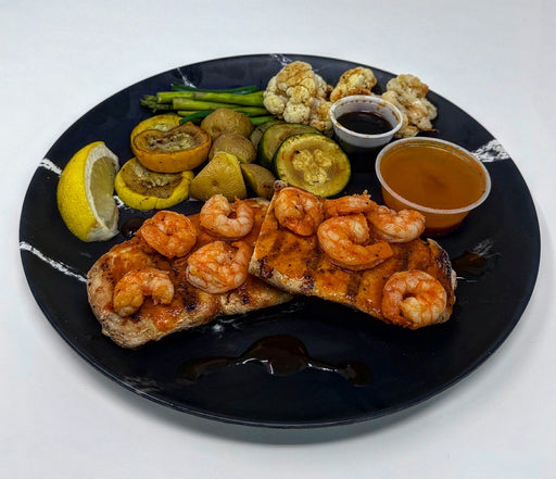 Plated dish with shrimp, bread, vegetables, and sauces on a black plate.