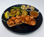 Plated dish with shrimp, bread, vegetables, and sauces on a black plate.