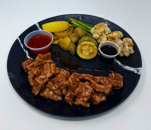 Plated dish with fried chicken, vegetables, and sauces on a black plate.