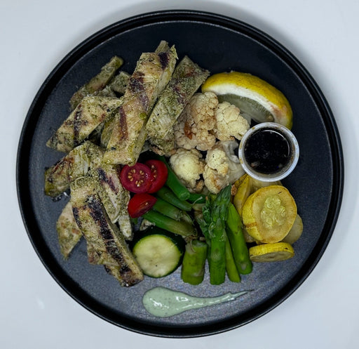 Plated dish with pesto chicken breast strips, vegetables, and sauces on a white background. Healthy meal made by Spartan Meal preps New Jersey.