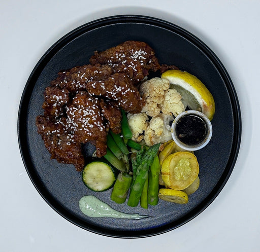 Platter of fried chicken with sides including vegetables and sauces on a white background.