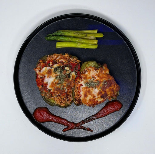 Two stuffed green peppers on a black plate with asparagus and a red sauce.