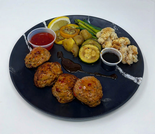Plated meal with meatballs, vegetables, and sauces on a black plate.