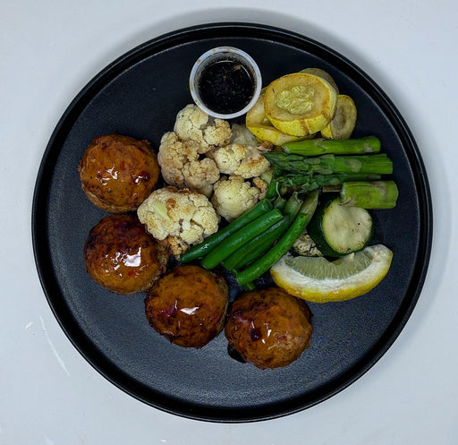 Plated dish with meatballs, vegetables, and a side of sauce on a black plate.