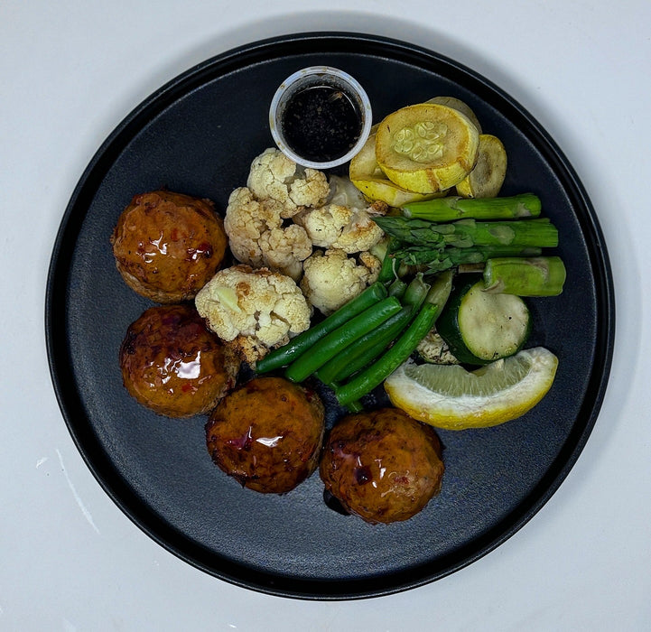 Plated dish with meatballs, vegetables, and a side of sauce on a black plate.