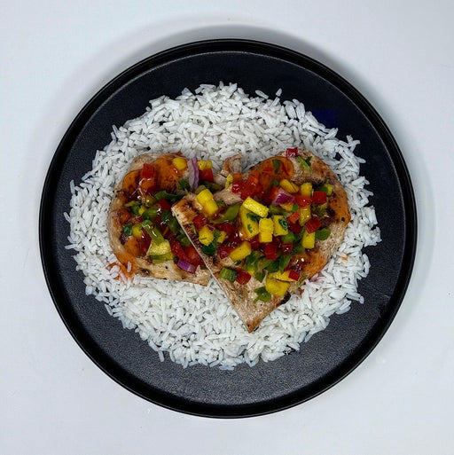Heart-shaped grilled chicken with pineapple salsa on a bed of rice on a black plate.