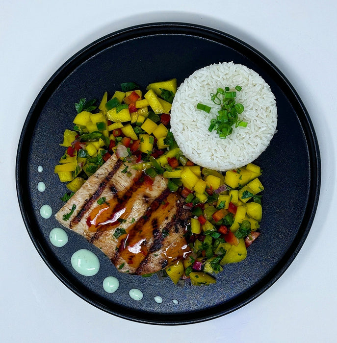 Heart-shaped grilled chicken with pineapple salsa on a bed of rice on a black plate.