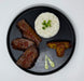 Black plate with grilled meat, white rice with green garnish, and fried plantains on a white background