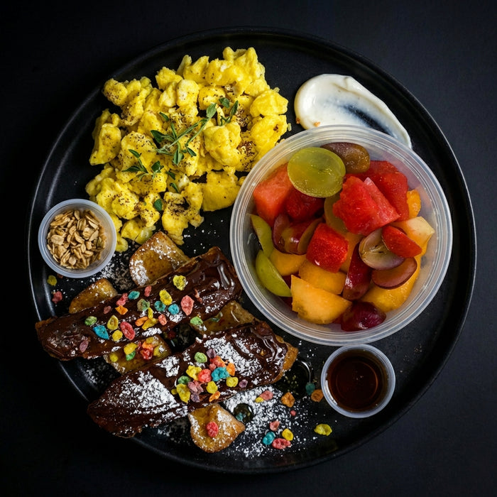 Breakfast platter with scrambled eggs, waffles, and fruit salad on a black plate, a meal made by Spartan Meal Preps New Jersey.