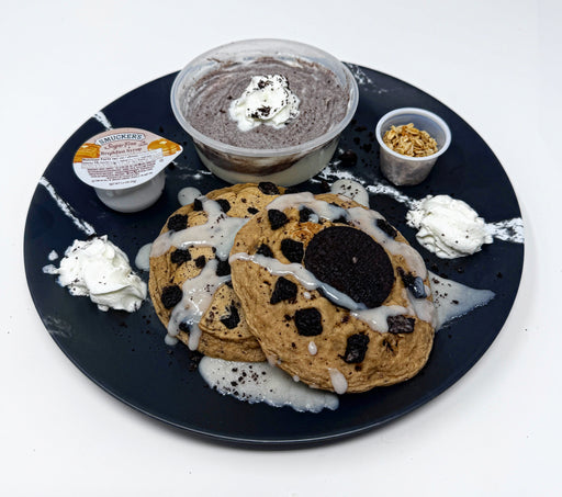 Cookies with cream on a black plate with small containers of cream and cookies.