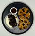 Two chocolate chip cookies on a black plate with a side of ice cream and syrup.