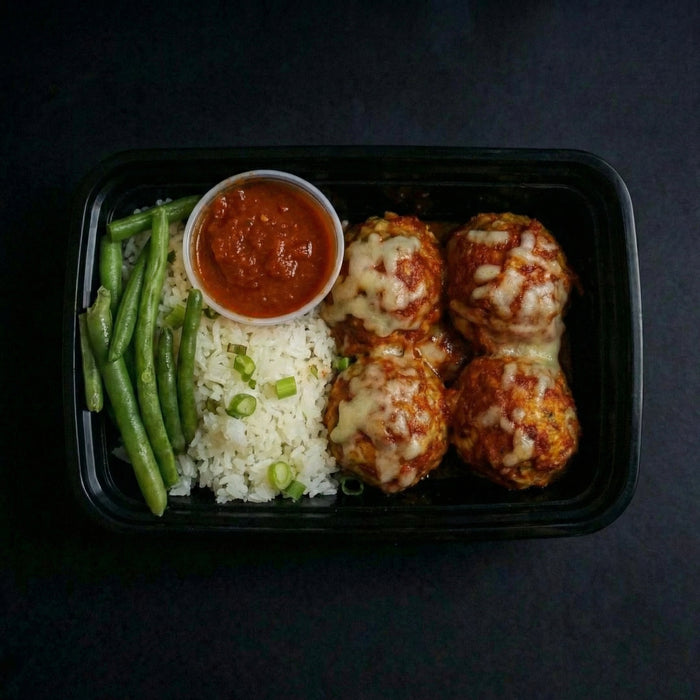 Plated meal with meatballs, green beans, rice, and a side of sauce on a dark background