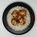 Plated dish with seafood on rice, garnished with green onions, on a white background