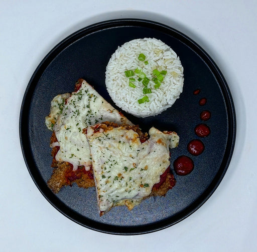 Plated dish with breaded meat, rice, and cherry tomatoes on a black plate.