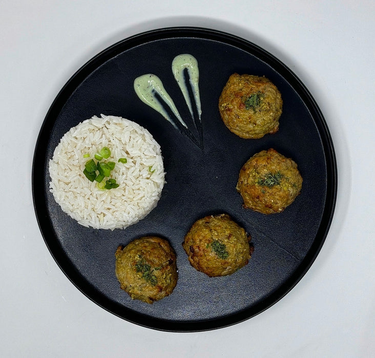 Black plate with rice and four green pesto chicken meat balls on a white background