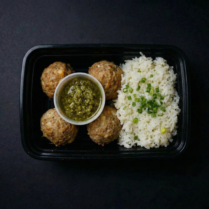 Plated meal with meatballs, rice, and a green sauce on a dark background