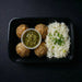 Plated meal with meatballs, rice, and a green sauce on a dark background