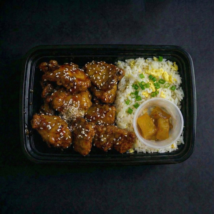 Takeout container with fried chicken, rice, and a side of sauce on a dark background