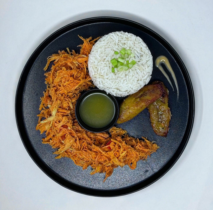 Plated dish with rice, fried plantains, and shredded carrots on a black plate.
