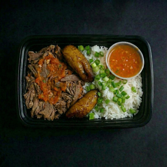 Plated meal with shredded meat, plantains, rice, and a side of sauce on a dark background