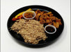 A plate with shredded BBQ chicken, sweet potato cubes, and grilled asparagus, served with condiments.