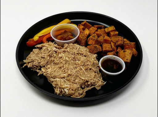 A plate with shredded BBQ chicken, sweet potato cubes, and grilled asparagus, served with condiments.