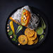 A styled overhead food shot of a wrap or burrito on patterned paper, served with round fried chips, green chutney, sauce drizzles, and herbs on a black plate against a dark background.