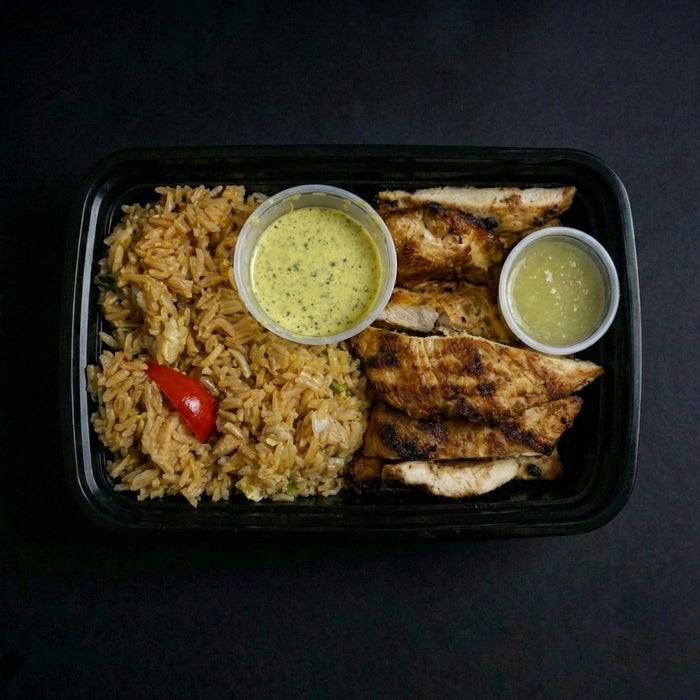 Plated meal with rice, grilled chicken, and two small bowls of dipping sauces on a dark background