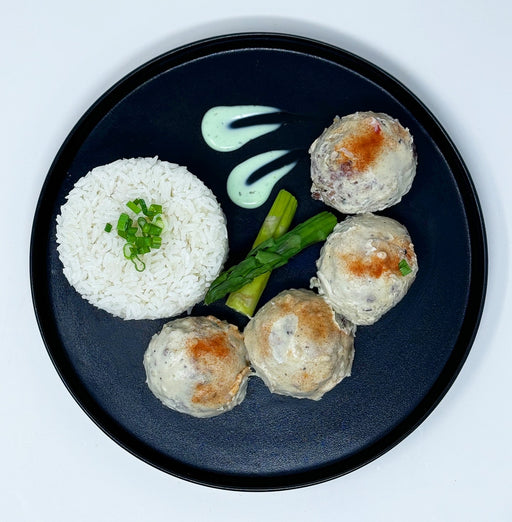 Four meatballs with green beans and red sauce on a bed of white rice in a black bowl.