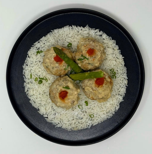 Four meatballs with green beans and red sauce on a bed of white rice in a black bowl.